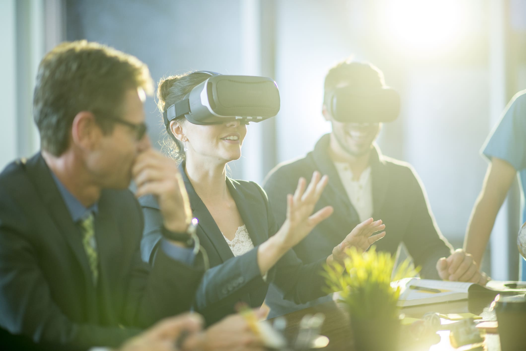 Petit groupe de spécialistes du commerce souriants qui sont assis dans une salle de conférence et essaient des casques de réalité virtuelle.